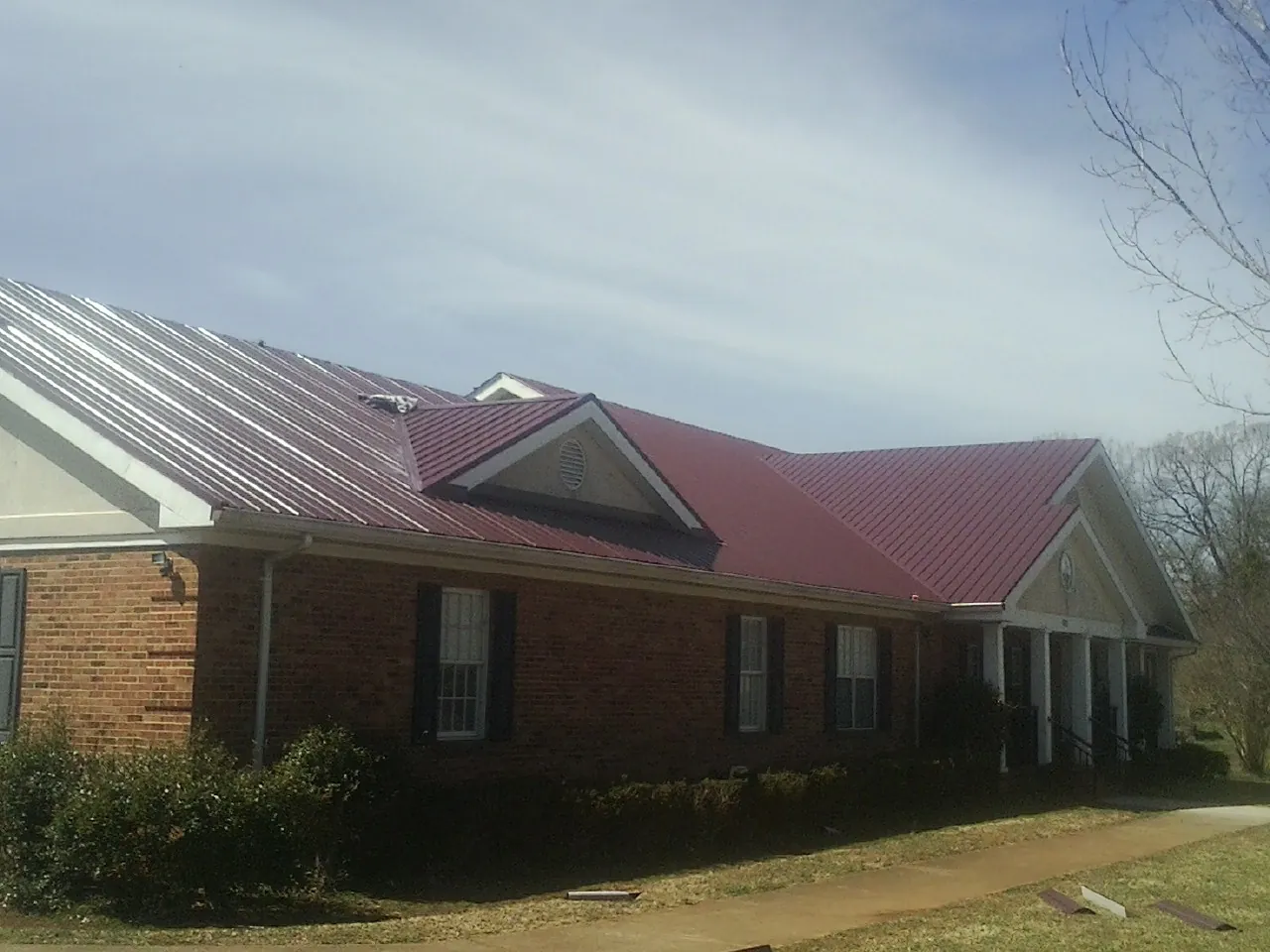 Red metal roof with gabled entries on a long brick building, from a Hail Damage Roof Repair job in Remlap