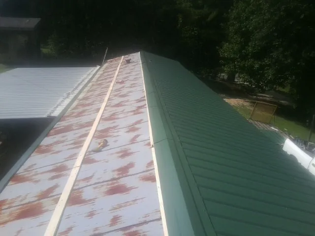 Old rusted panels beside newly installed green metal roofing — Wind Damage Roof Repair by Roofing Brothers in Remlap