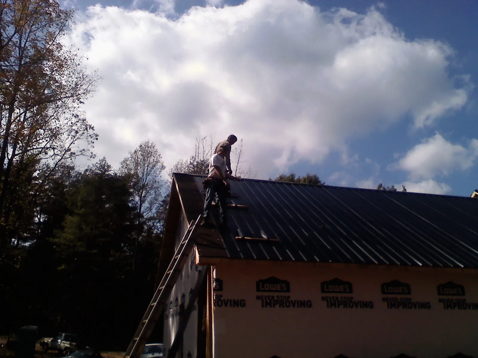 Roofer fastening dark metal panels high against a cloudy sky, from a Roof Inspection job in Remlap